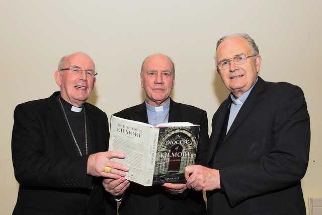Priests and bishop holding diocese of kilmore book